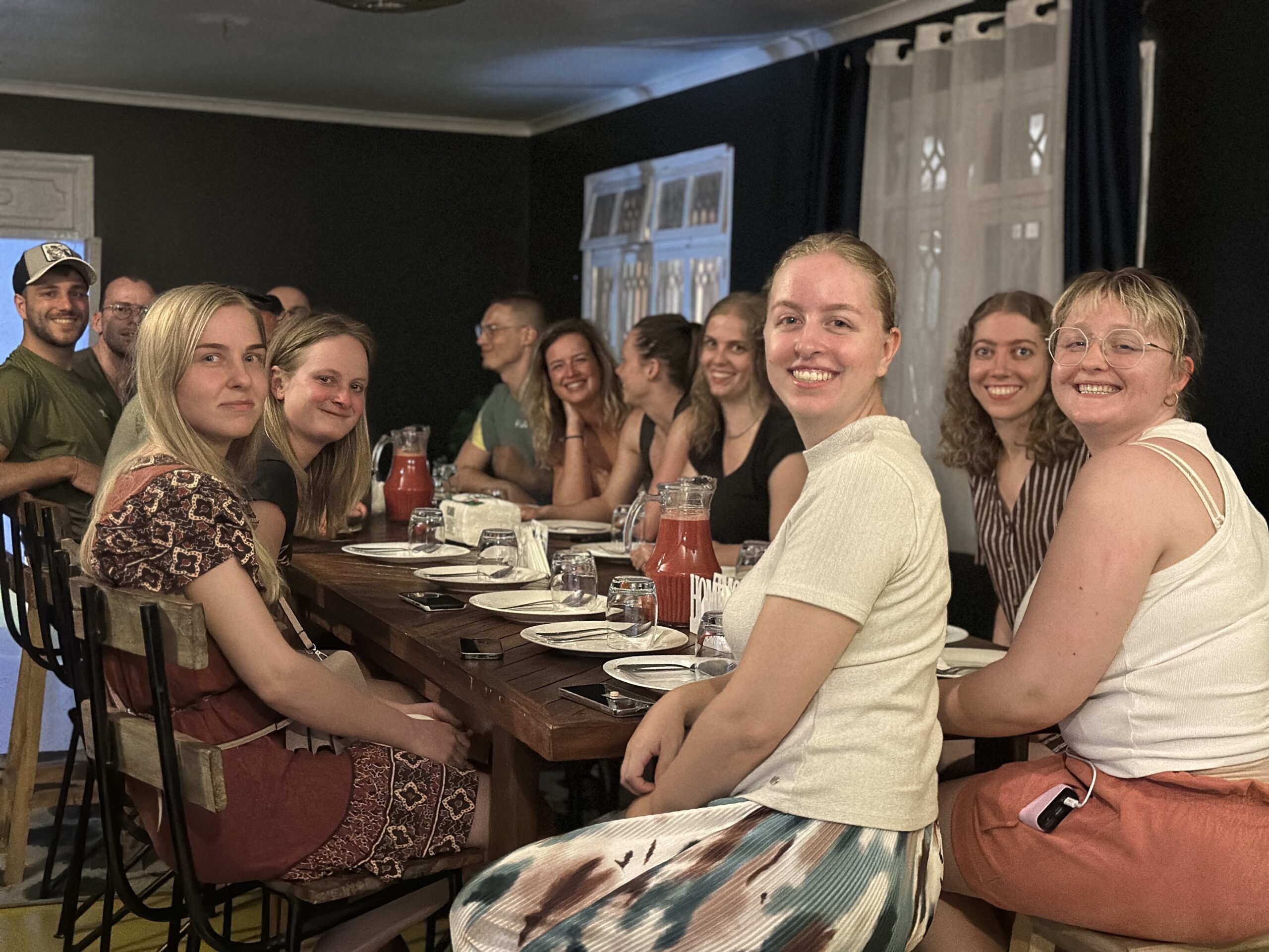 A group of Gallivanters Hostel guests smiling together around a dinner table in Dar es Salaam