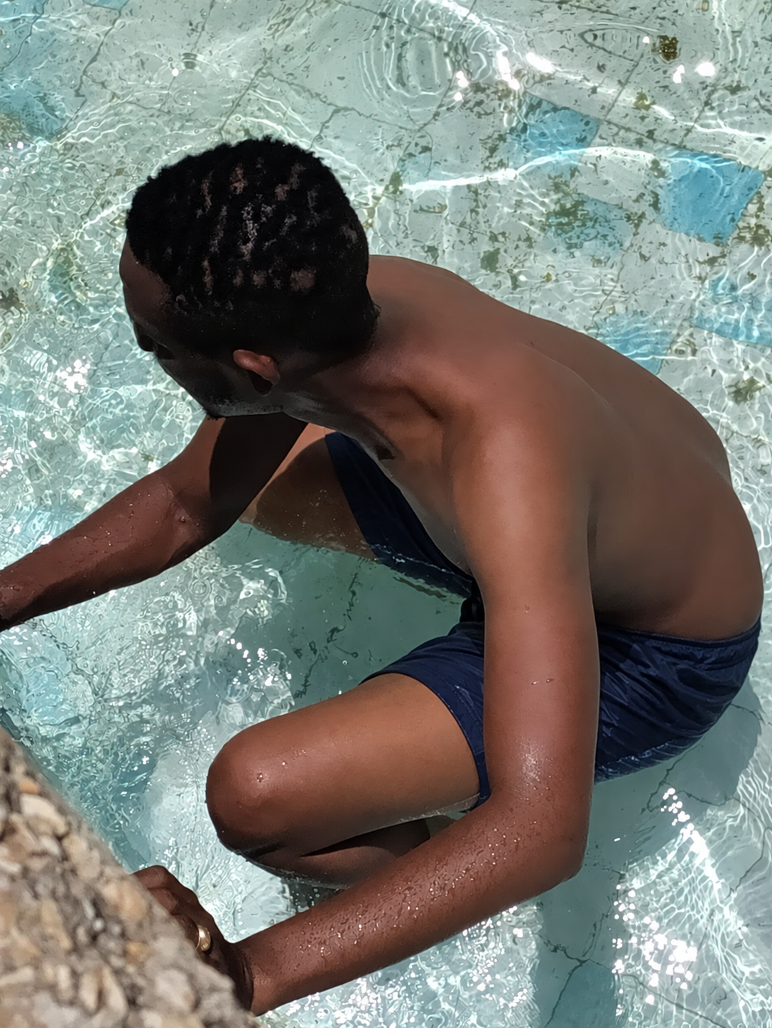 Kibwana wearing navy shorts while cleaning and repairing the Gallivanters Hostel pool