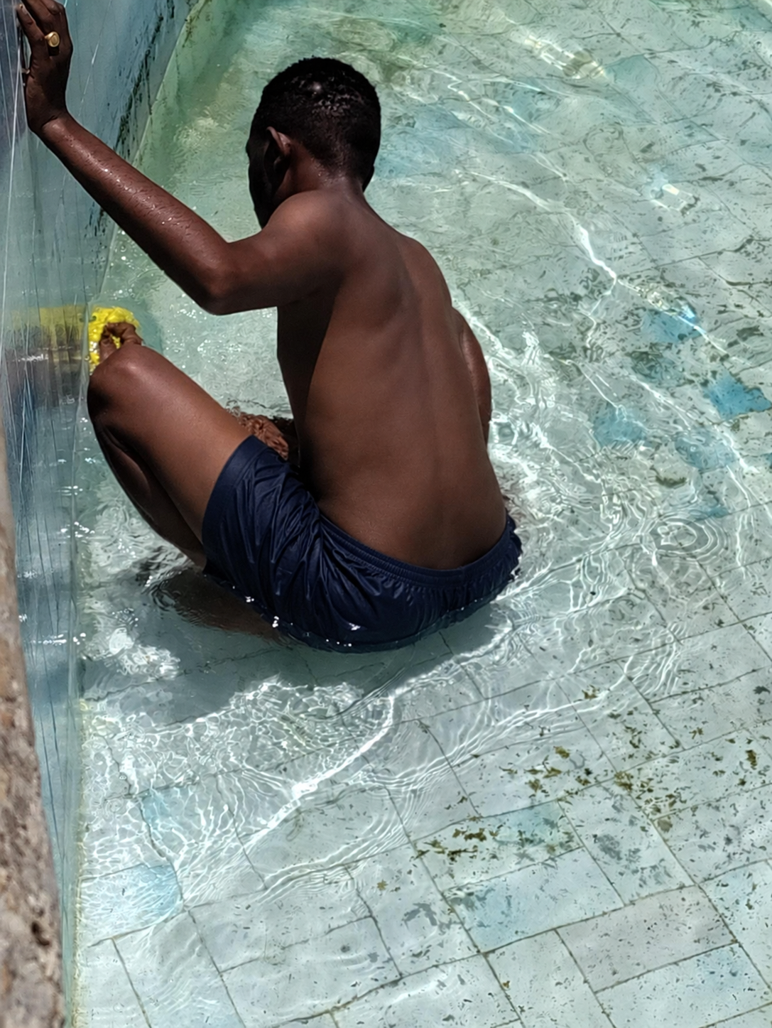 Kibwana wearing navy shorts while repairing the drained pool at Gallivanters Hostel
