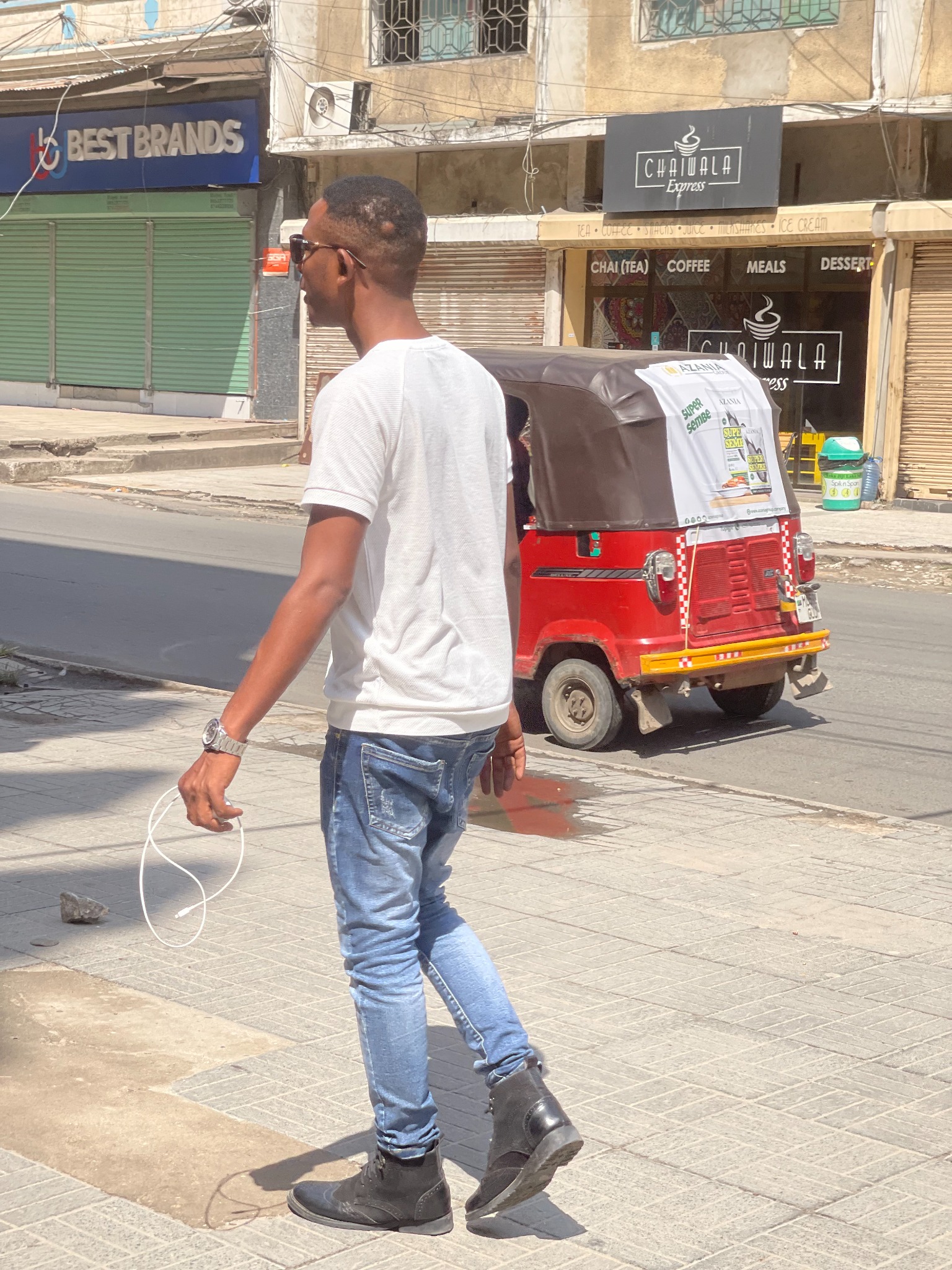 Kibwana walking along a Dar es Salaam street as a red bajaj passes behind him