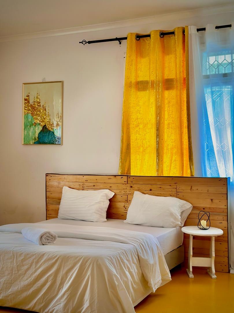 A made bed with white linens and yellow curtains in the last Gallivanters room to be packed up.