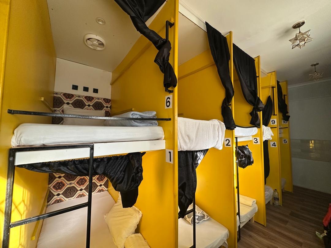 Yellow pod-style bunk beds with black privacy curtains in the ten-bed dormitory at Gallivanters Hostel.