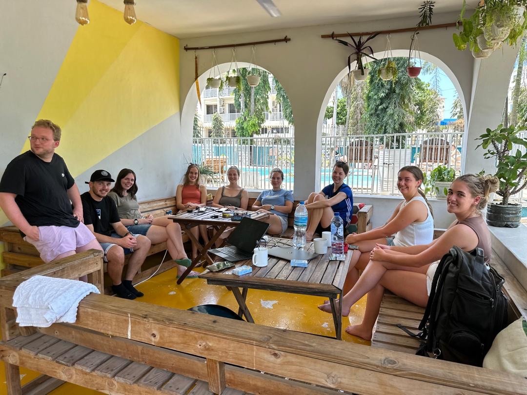 Travelers gathered around wooden tables in the shared lounge overlooking the pool at Gallivanters Hostel.
